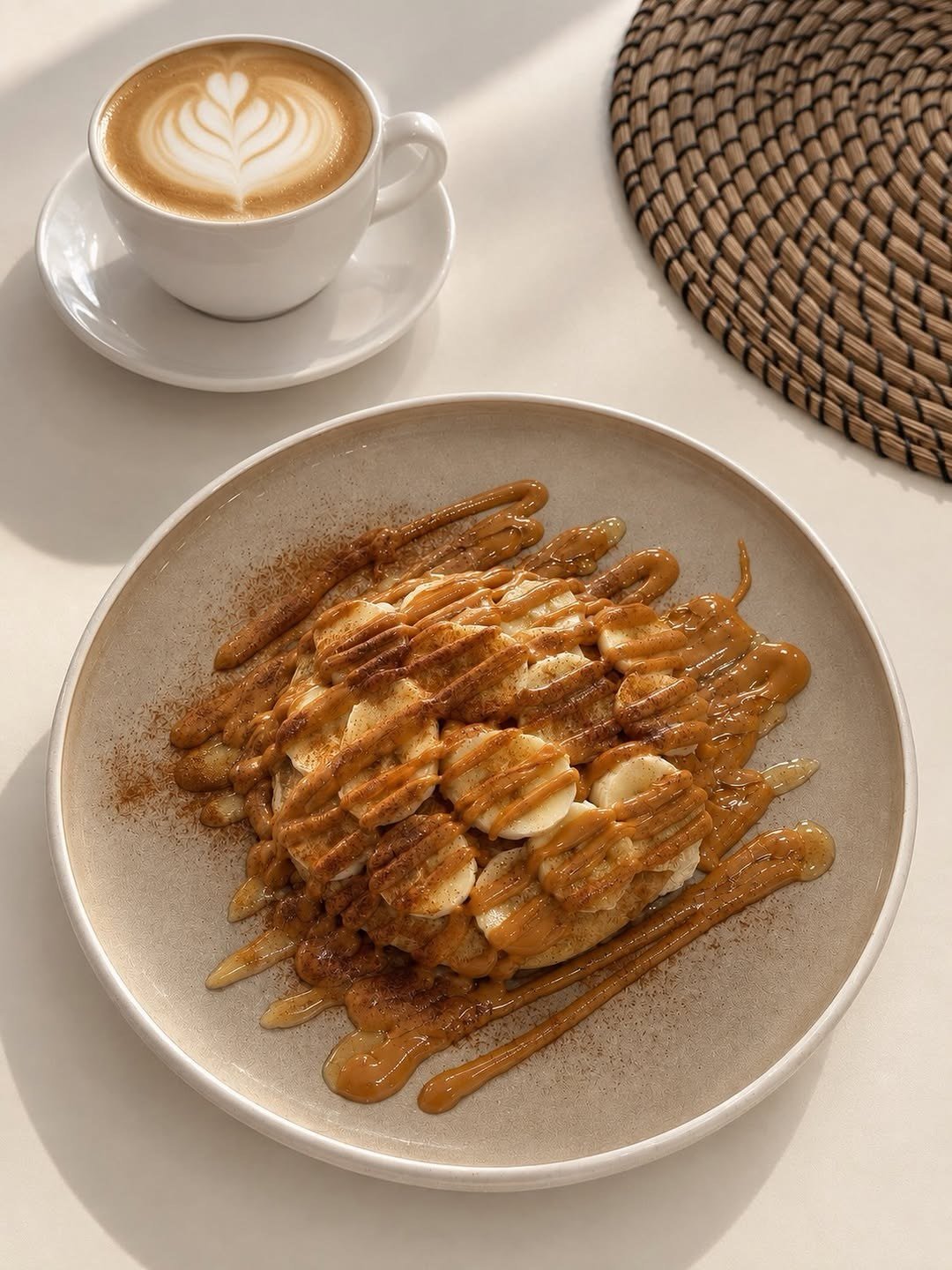 Panquecas cobertas com rodelas de banana e manteiga de amendoim, com um café com arte no leite ao lado