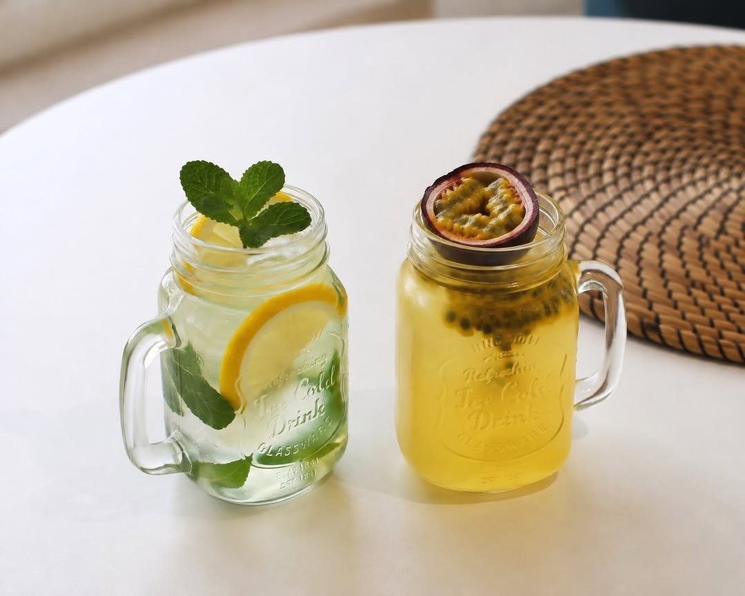Duas limonadas em frascos com asa, uma de limão com hortelã e outra de maracujá, numa mesa branca